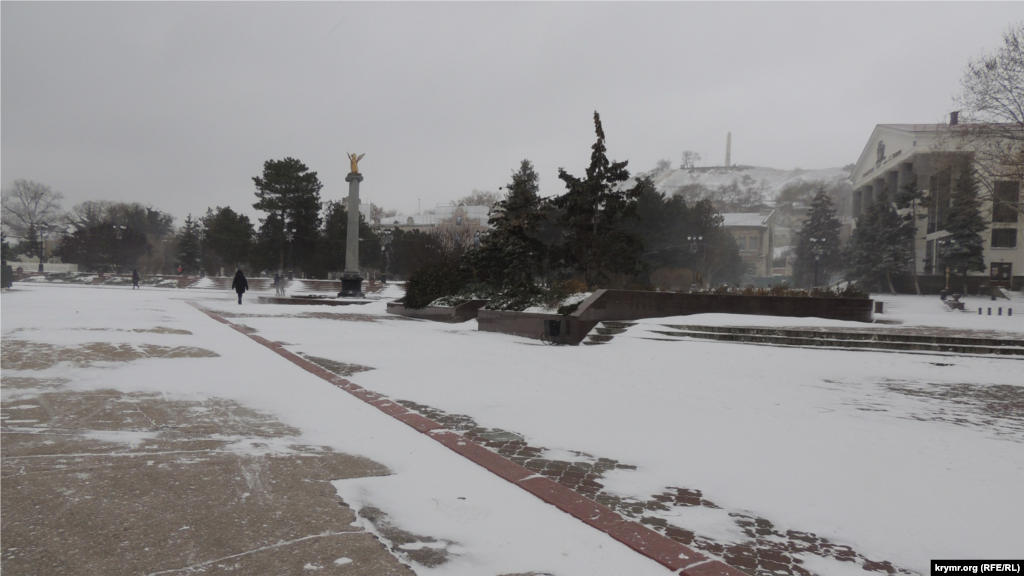 Золотистая стела с символом Керчи грифоном на вершине – одна из достопримечательностей города. У подножия стелы находятся капсулы с землей из городов-героев. Тем временем ветер начинает сдувать снежный покров с тротуаров. Сильные порывы ветра с моря – наиболее частая причина, почему снег в Керчи «не залеживается»