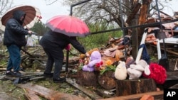 Жени положуваат цвеќе врз урнатините на уништената куќа каде што три деца беа убиени во руски напад во Житомир на 26 мај 2025 година