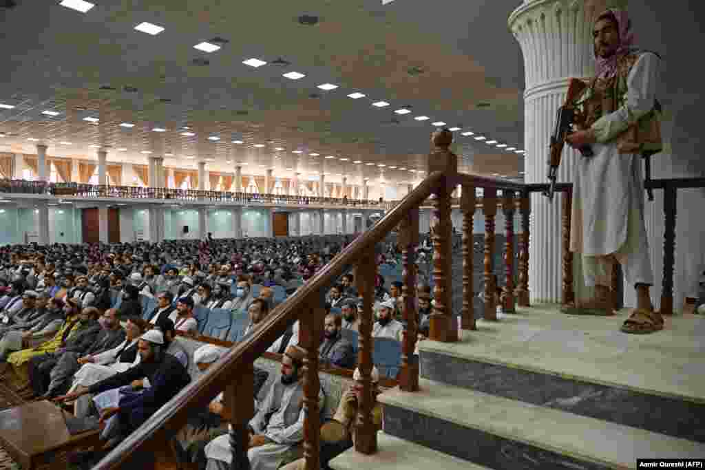 A fighter wearing sandals stands guard as senior Taliban figure Abdul Baqi Haqqani addresses an all-male meeting on the Taliban's education policies at Kabul's Loya Jirga Hall on August 29.